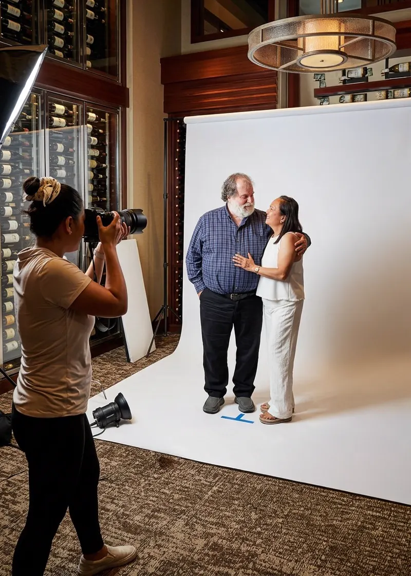 A Hey You Booth photographer takes a portrait of a smiling couple on a white backdrop set up at a venue